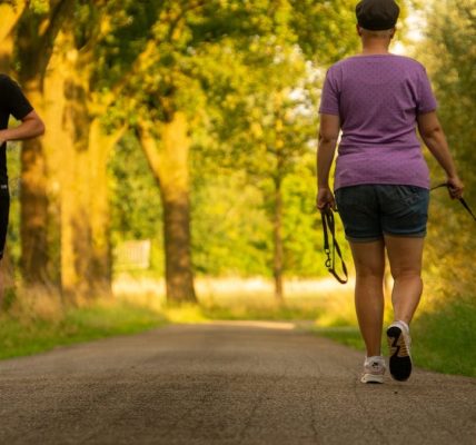 Man jogging and woman walking a dog on a picturesque outdoor path.