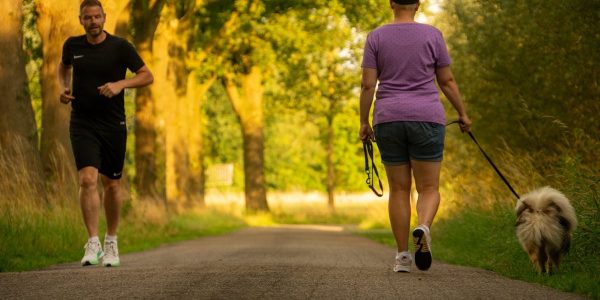 Man jogging and woman walking a dog on a picturesque outdoor path.